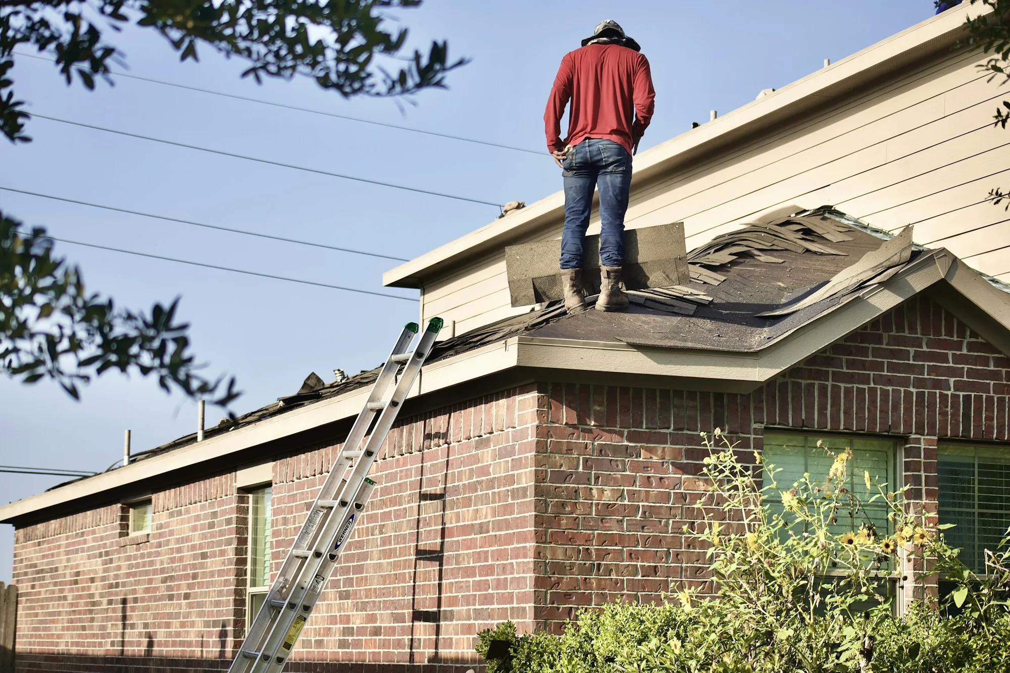 Roofer standing on a residential roof beside an extension ladder