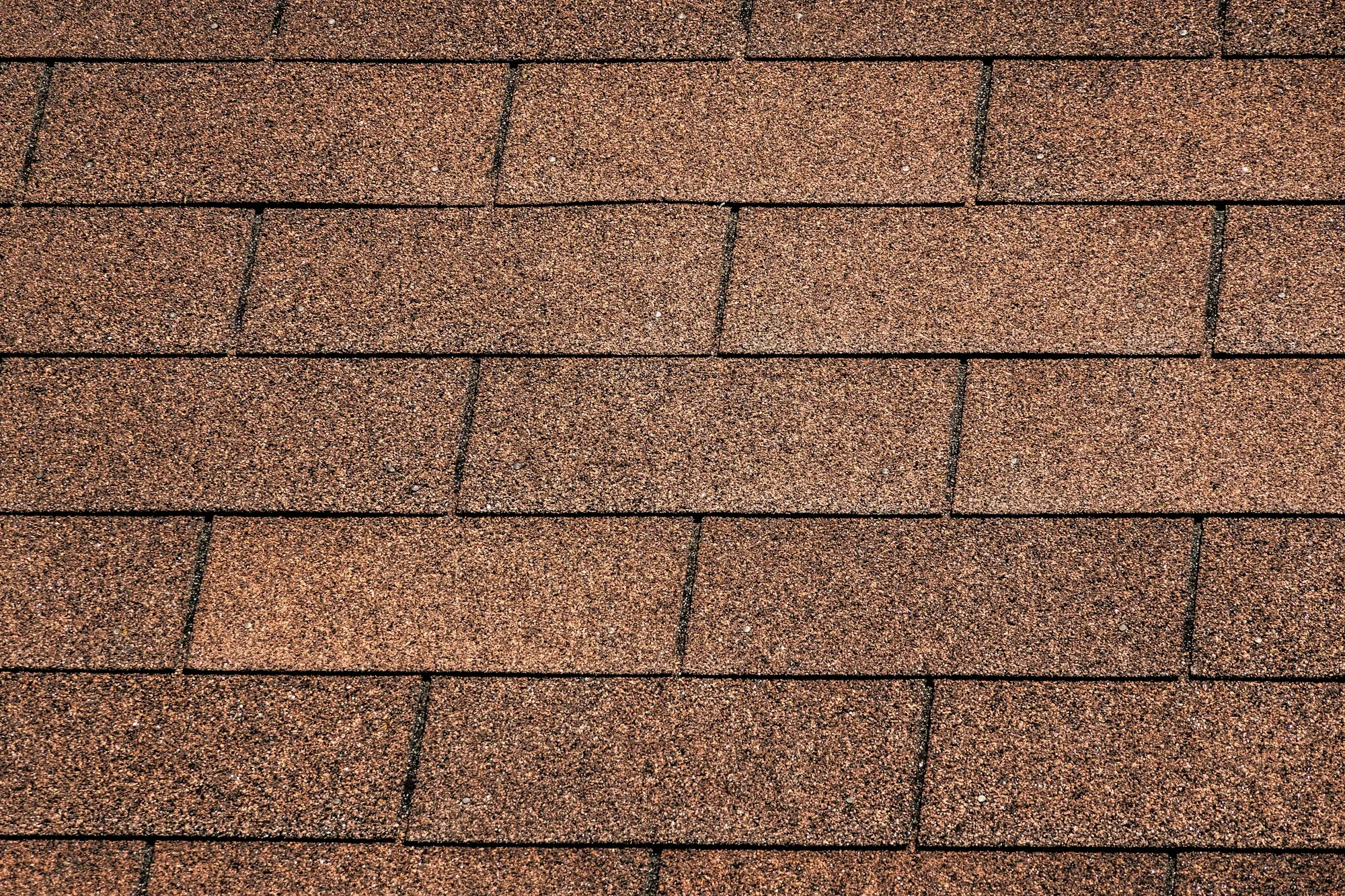 Overlapping courses of brown asphalt roof shingles seen close up