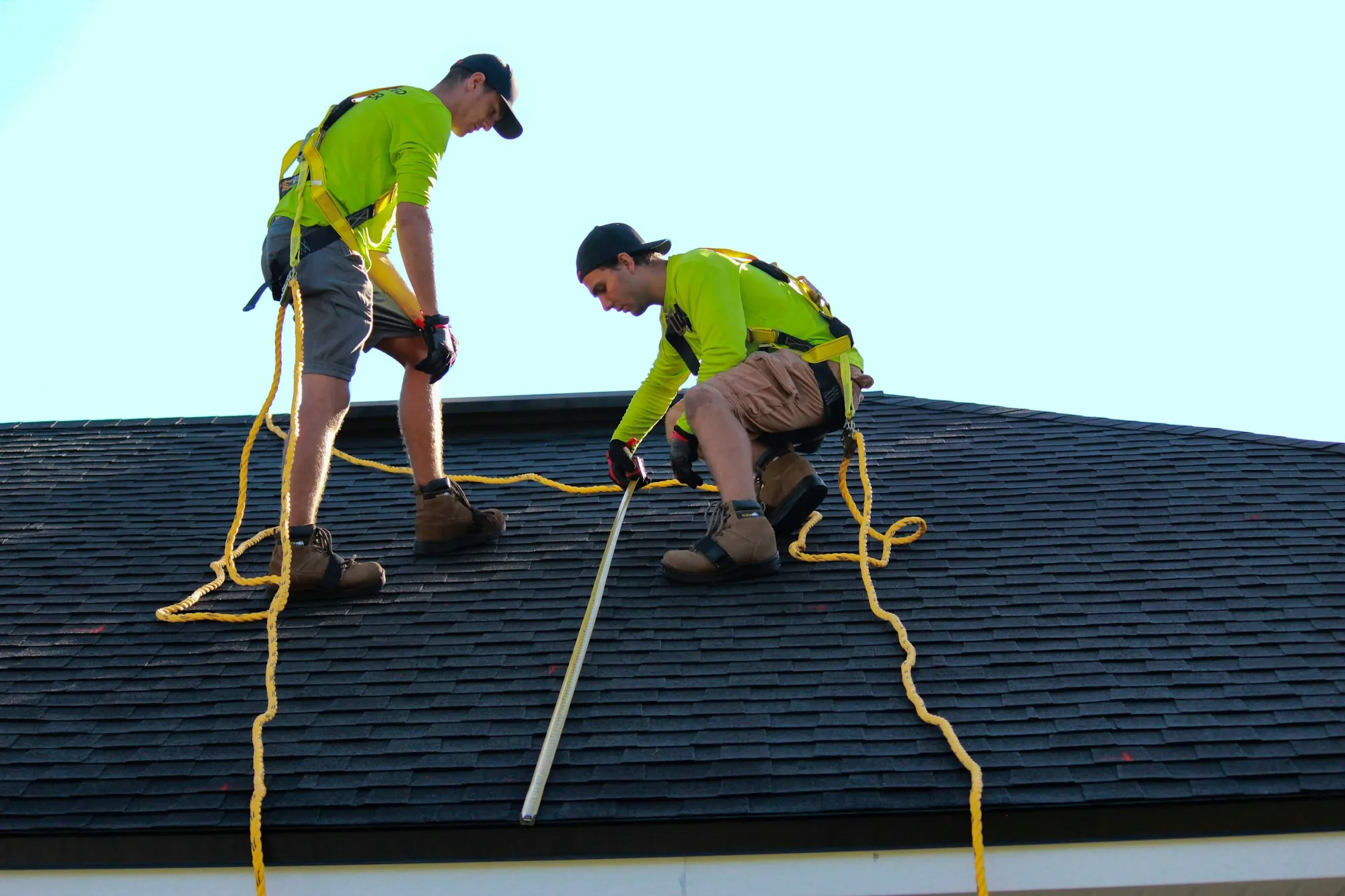 Two roofers measuring and checking a residential asphalt shingle roof