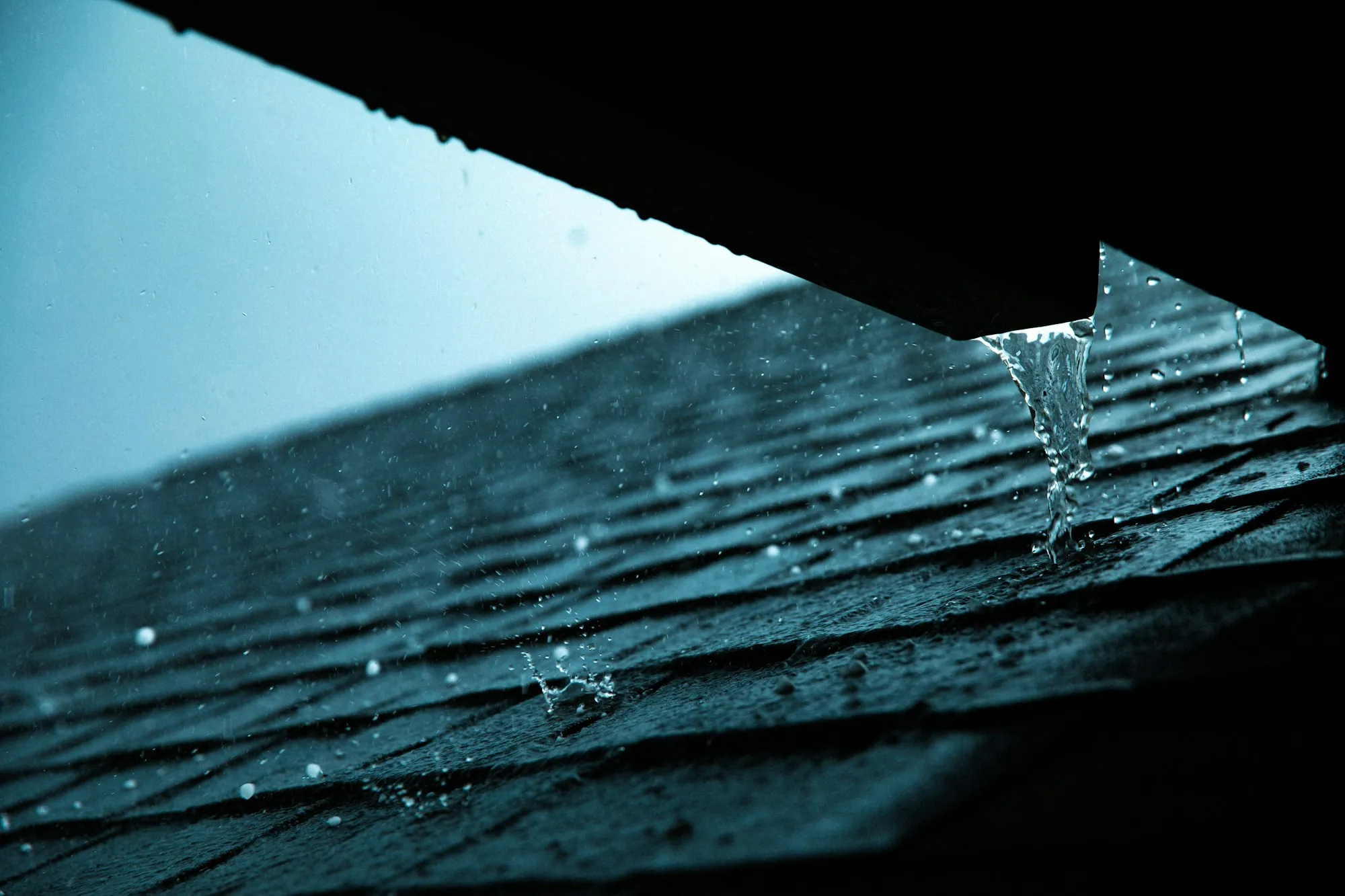 Rainwater running off the edge of a dark asphalt shingle roof