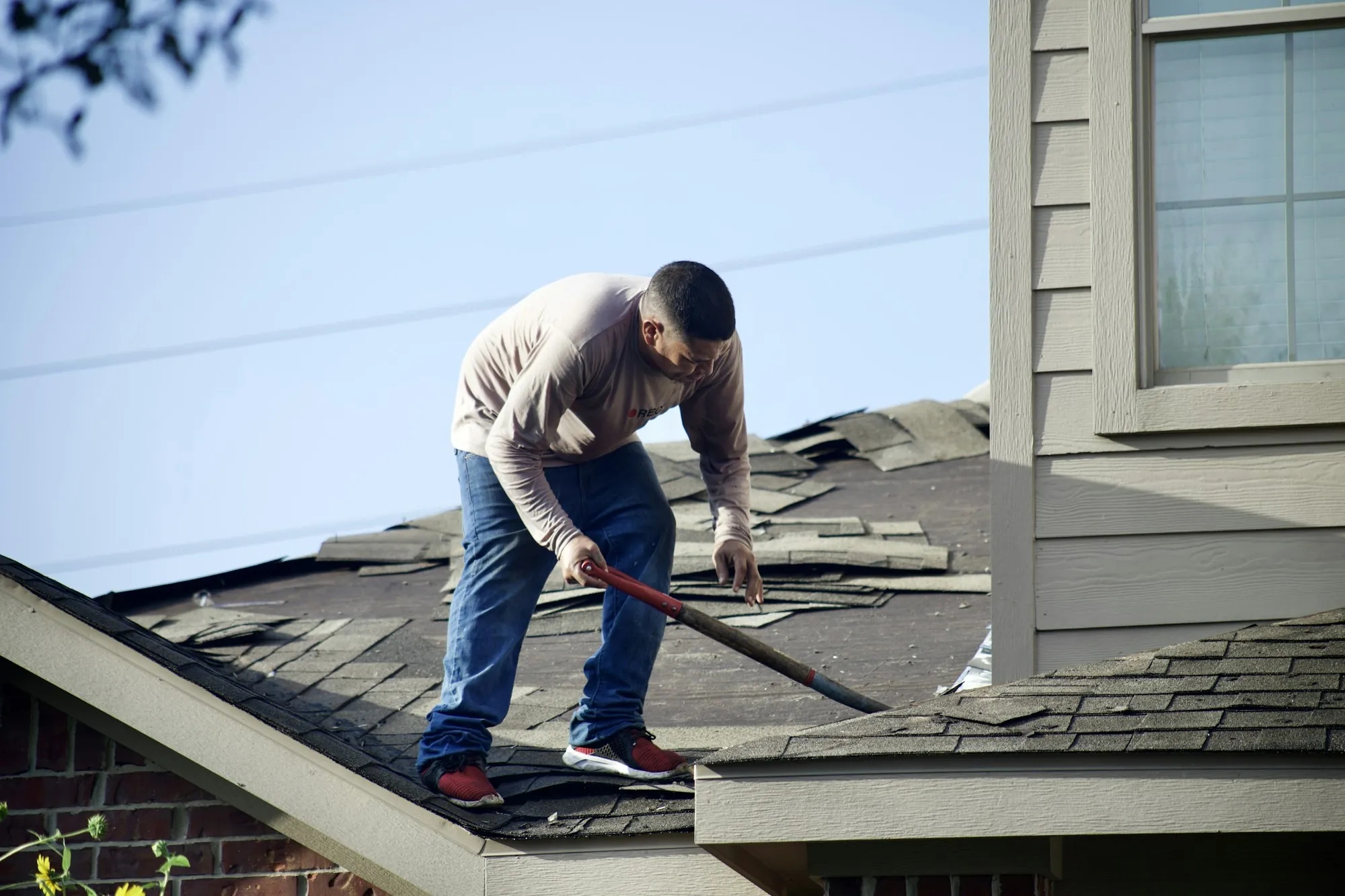 Roofer stripping old shingles from a residential roof with a tear-off shovel